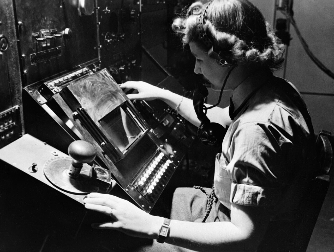 A uniformed woman seated at a radar console, marking positions from a round cathode-ray screen.