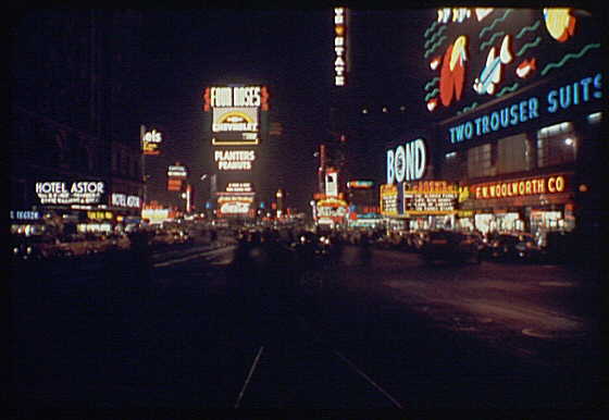 Color night photograph of Times Square with illuminated billboards for Four Roses, Bond, and Woolworth.