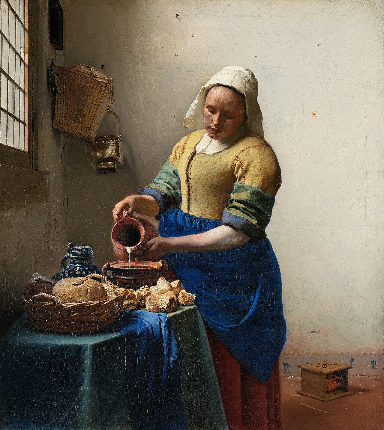 Painting of a woman in a yellow bodice and blue apron pouring milk from a jug into a bowl beside a window, intent on her work.